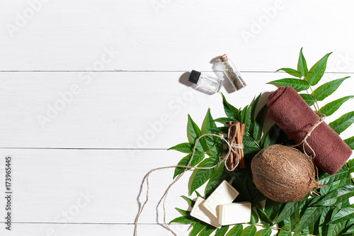 Natural handmade soaps with oil, brown towel, coconut and green leaves on white wooden background