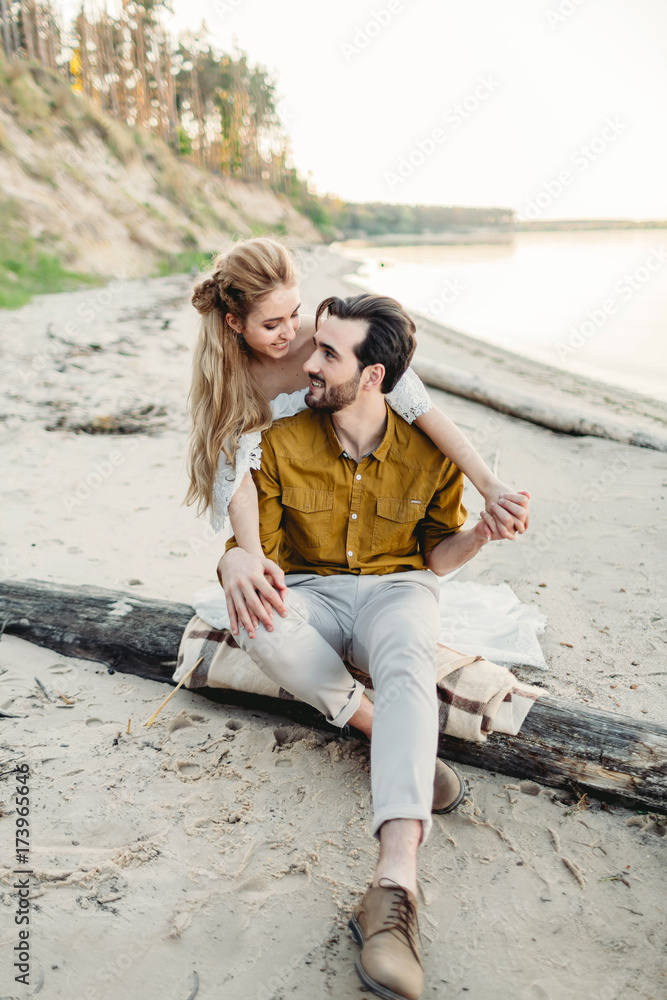 A young couple is having fun and hugging on the beach. Beautiful girl embrace her boyfriend from back. Wedding walk. A newlyweds looks at each other. Artwork A young couple is having fun and hugging on the beach. Beautiful girl embrace her boyfriend from back. Wedding walk. A newlyweds looks at each other. Artwork