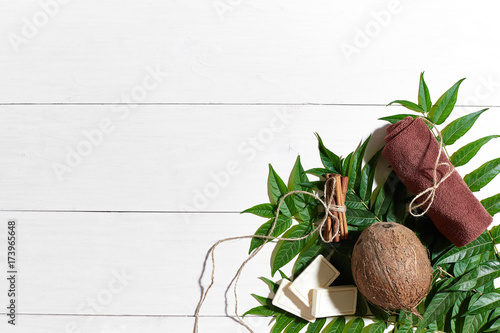Natural handmade soaps with cinnamon, brown towel, coconut and green leaves on white wooden background