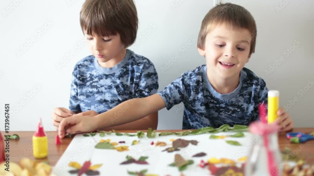 Sweet children, boys, applying leaves using glue while doing arts and crafts in school, autumn time Sweet children, boys, applying leaves using glue while doing arts and crafts in school, autumn time