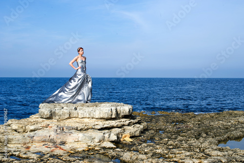 beautiful fashion model standing on rocks with grey evening gown