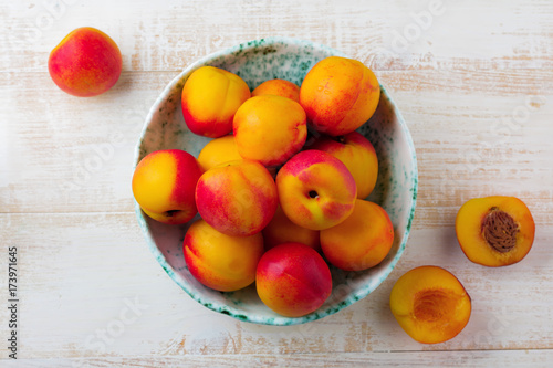 Fresh juicy fruit nectarines in ceramic bowl  on  white wooden background. Selective focus. Top view. Rustic style.