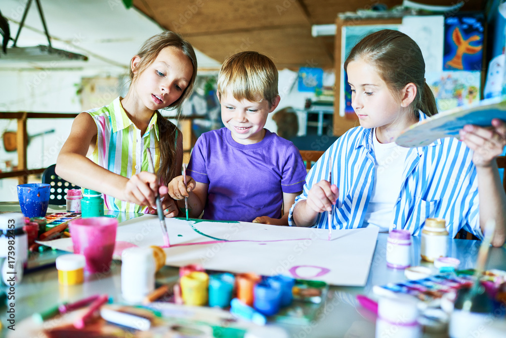 Naklejka premium Portrait of three children painting picture together smiling happily while working in art studio during lesson
