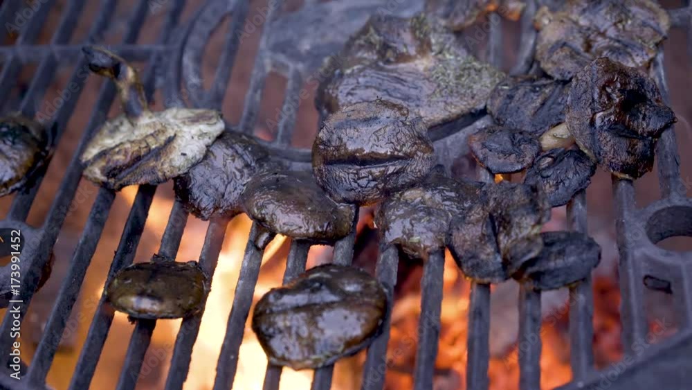 Shiitake mushrooms on a grill with yellow flames below and smoke rising