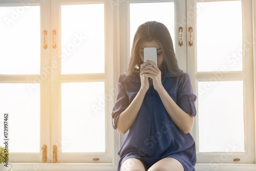 Beautiful woman praying and holding phone in the morning on windowsill .Religion, Spirituality and Prayer concept