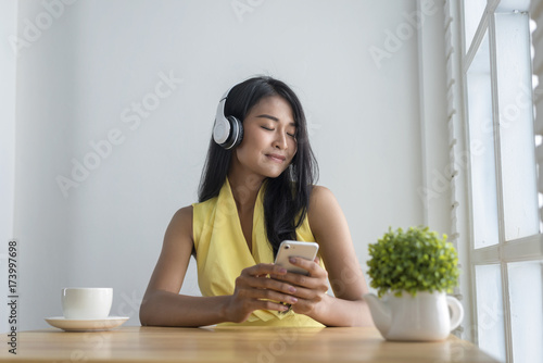 Asian women sitting to relax and listening music in wireless headphones at the cafe,holding smartphone in hand