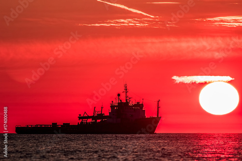 Travel destination. Red dawn at sea. Fishing trawler boat silhouette on tropical waters at sunrise.