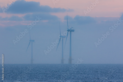 Tranquil environment scene at sea. Offshore wind farm turbines on a misty morning at sunrise
