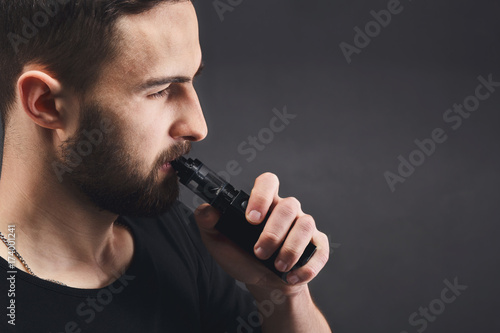 Young man vaping e-cigarette on black