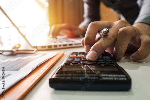 businessman hand working with finances about cost and calculator and laPtop with tablet and smartphone on withe desk in modern office in morning light