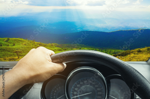 View on the dashboard of the truck driving.The driver is holding the steering wheel. Mountain landscape is in front of the car.