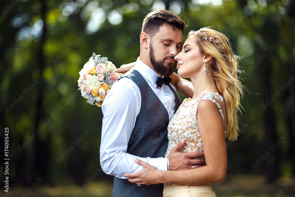 Fototapeta premium Stylish couple of happy newlyweds posing in the park on their wedding day. Perfect couple bride, groom posing and kissing 