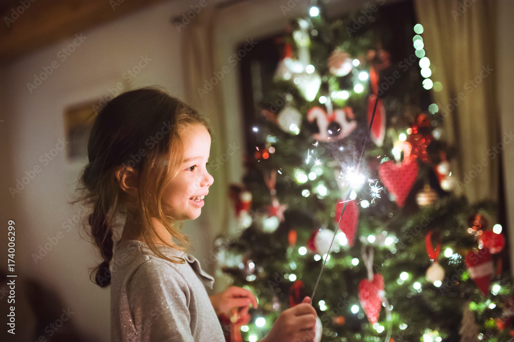 Little girl with a sparkler in front of Christmas tree. Little girl with a sparkler in front of Christmas tree.