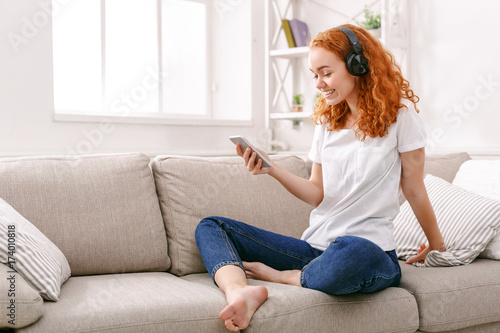 Happy young woman in headphones on beige couch