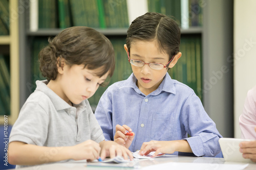 Portrait of two boy writing on paper at classroom together, Children with education concept.