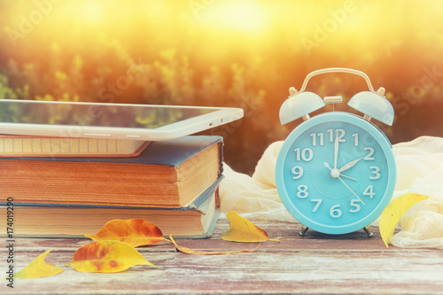 Image of autumn Time Change. Fall back concept. Dry leaves and vintage alarm Clock on wooden table outdoors at afternoon photo