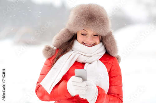 happy woman in winter fur hat with smartphone
