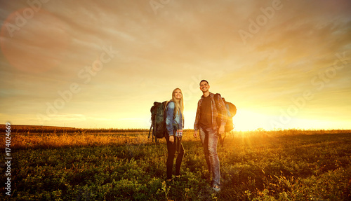 A couple of tourists with backpacks on nature at sunset.