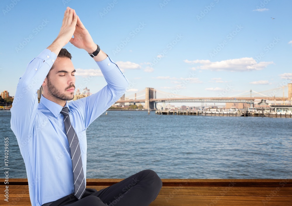 Business man meditating against water and skyline Business man meditating against water and skyline