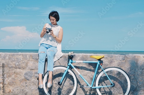 Asian woman with vintage bicycle over blue sky background and beach. © Mallika