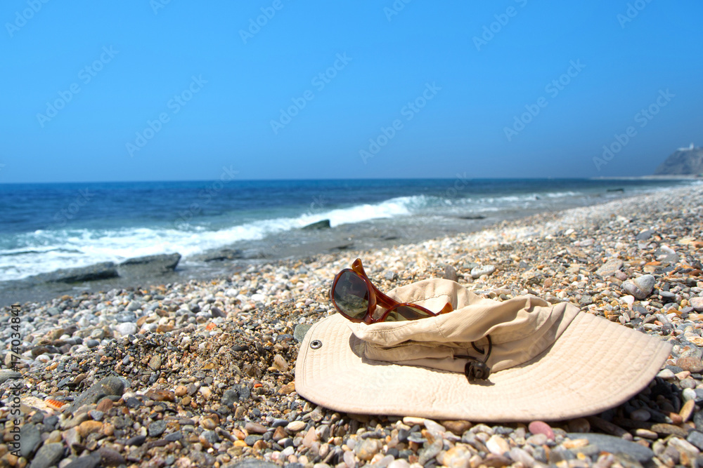 Old hat and sunglasses on the pebble beach of the Mediterranean Sea Old hat and sunglasses on the pebble beach of the Mediterranean Sea