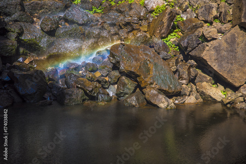 Magical Rainbow created by waterfall fallin on stone formation situated next to a water hole.