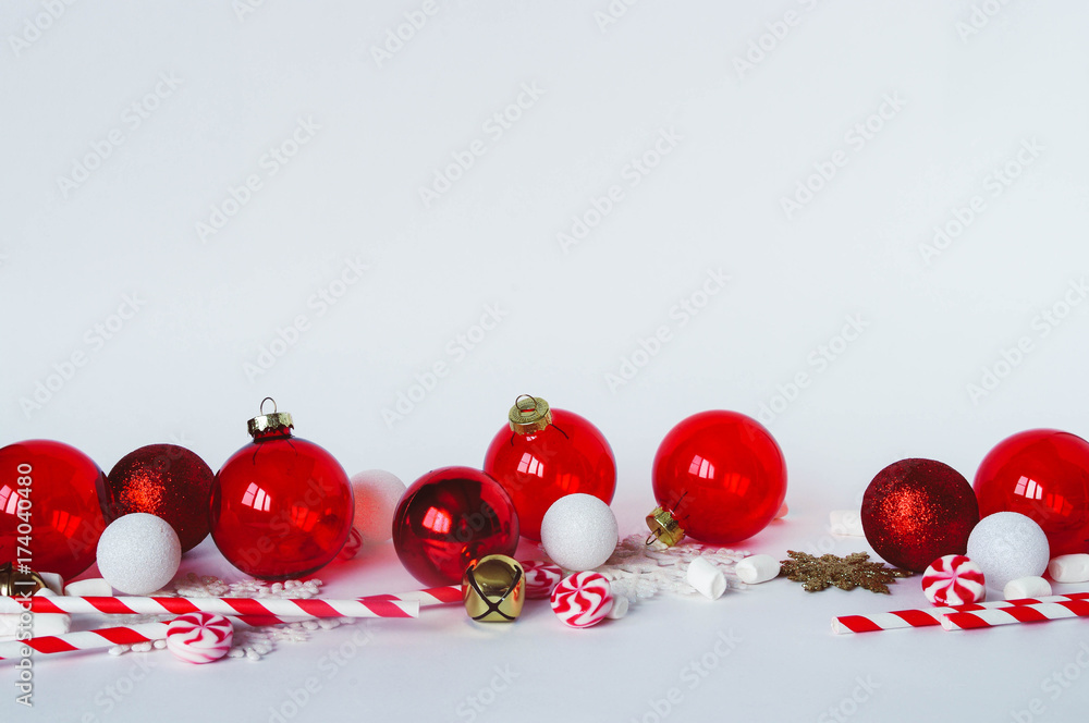 Christmas decorations on white background. Transparent red and glitter baubles ornaments, peppermint swirl candy, gold bells, marshmallow and striped paper straws Christmas decorations on white background. Transparent red and glitter baubles ornaments, peppermint swirl candy, gold bells, marshmallow and striped paper straws