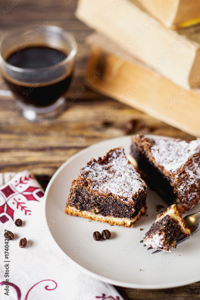 sweets and desserts, pastries, delicious chocolate cake with poppy seeds, raisins and powdered sugar with a cup of black coffee on a dark wooden background sweets and desserts, pastries, delicious chocolate cake with poppy seeds, raisins and powdered sugar with a cup of black coffee on a dark wooden background