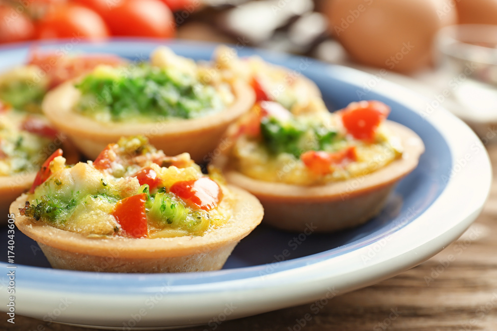 Plate with broccoli quiche tartlets on wooden table