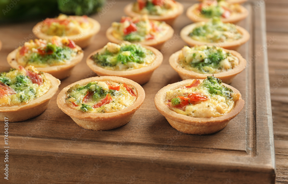 Board with broccoli quiche tartlets on wooden table Board with broccoli quiche tartlets on wooden table