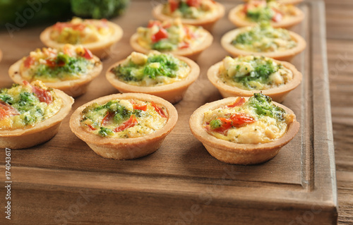 Board with broccoli quiche tartlets on wooden table