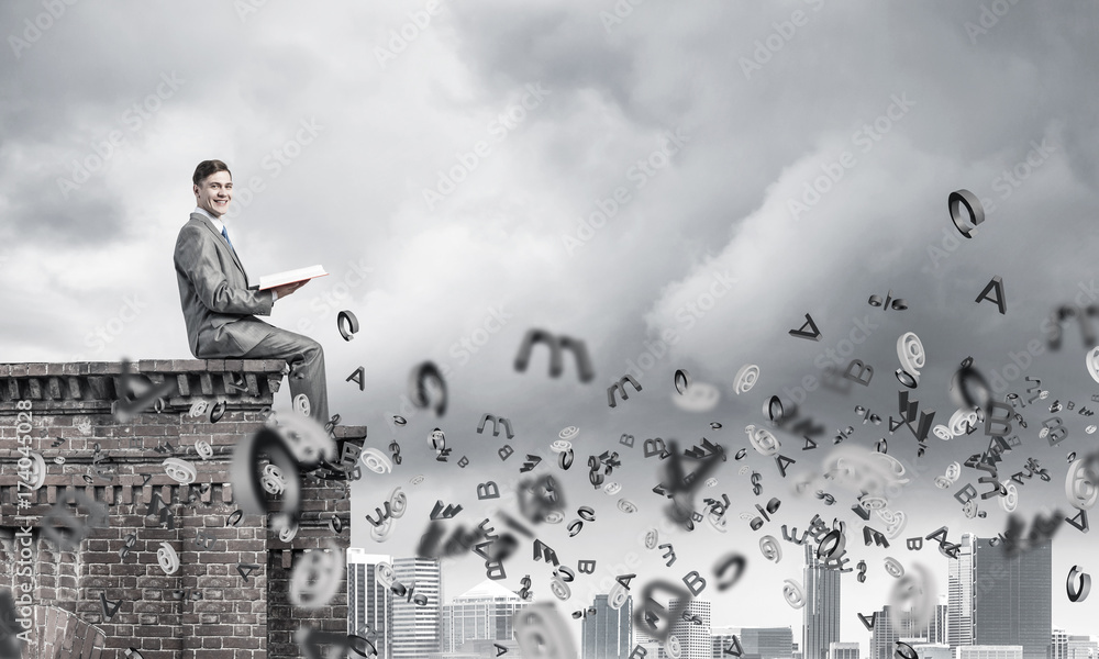 Man on roof edge reading book and symbols flying around Man on roof edge reading book and symbols flying around