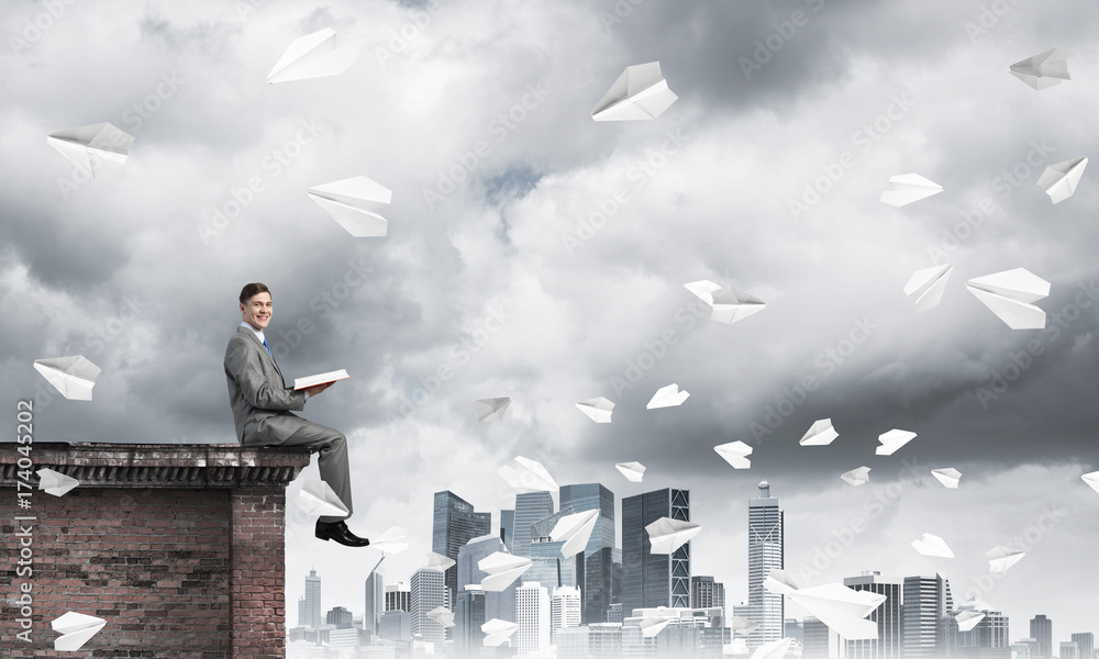 Man on roof edge reading book and cityscape at background Man on roof edge reading book and cityscape at background