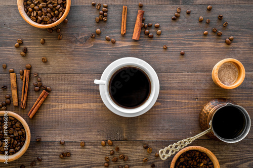 Cup of black coffee near coffee beans and cinnamon on wooden background top view