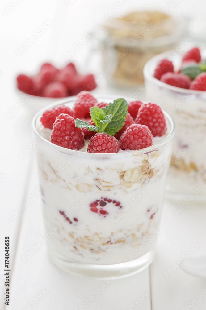 Sweet dessert with yogurt, raspberries and oats in glasses on white wooden table. Sweet dessert with yogurt, raspberries and oats in glasses on white wooden table.