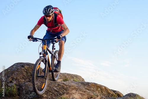 Cyclist in Red Riding the Bike Down the Rock on the Blue Sky Background. Extreme Sport and Enduro Biking Concept.