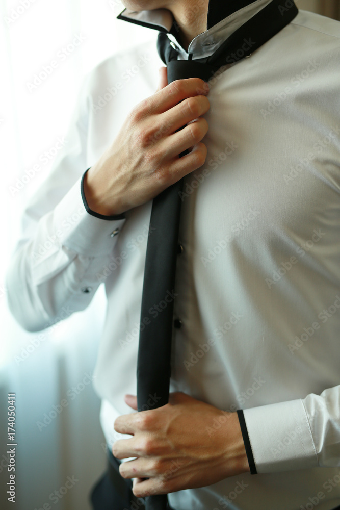a man adjusting his black tie against a white shirt