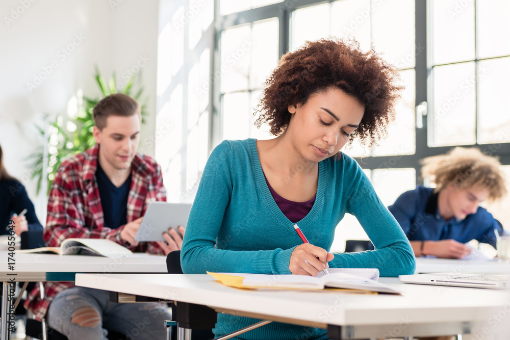 Young female student with a serious facial expression concentrating while writing an essay during class in an international university Young female student with a serious facial expression concentrating while writing an essay during class in an international university