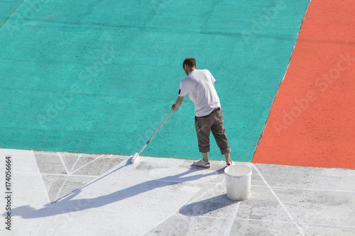 Man at work. Road worker painting asphalt. Worker painting white, red, aquamarine color on the street surface.