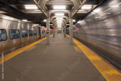 Long Exposure of high speed train passing station platform waiting departing train at railroad terminal hub