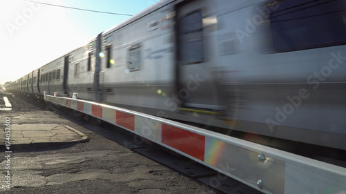 Commuter train travel past railroad crossing gate at high speed motion blur. Flashing lights warn car traffic of oncoming train