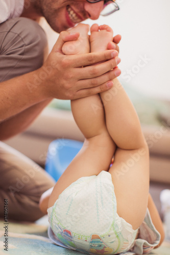 The young happy father lifting feet of his little son in the room