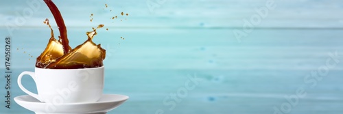 Obraz na plátne Coffee being poured into white cup against blurry blue wood