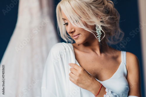 The portrait of the young bride at a window - the girl prepares for a wedding and dresses accessories, earrings. The face of the blonde with a stylish hairstyle