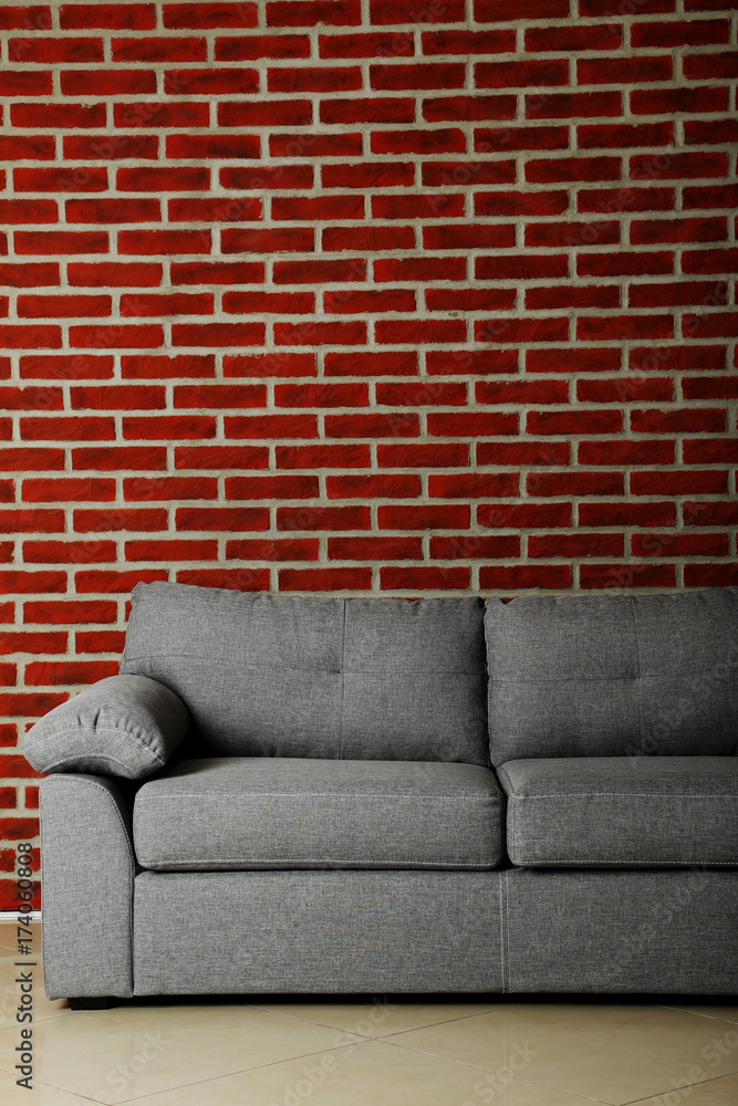Naklejka premium Grey sofa on a red brick wall background