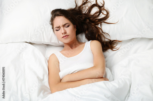 Sick young woman lying in white bed