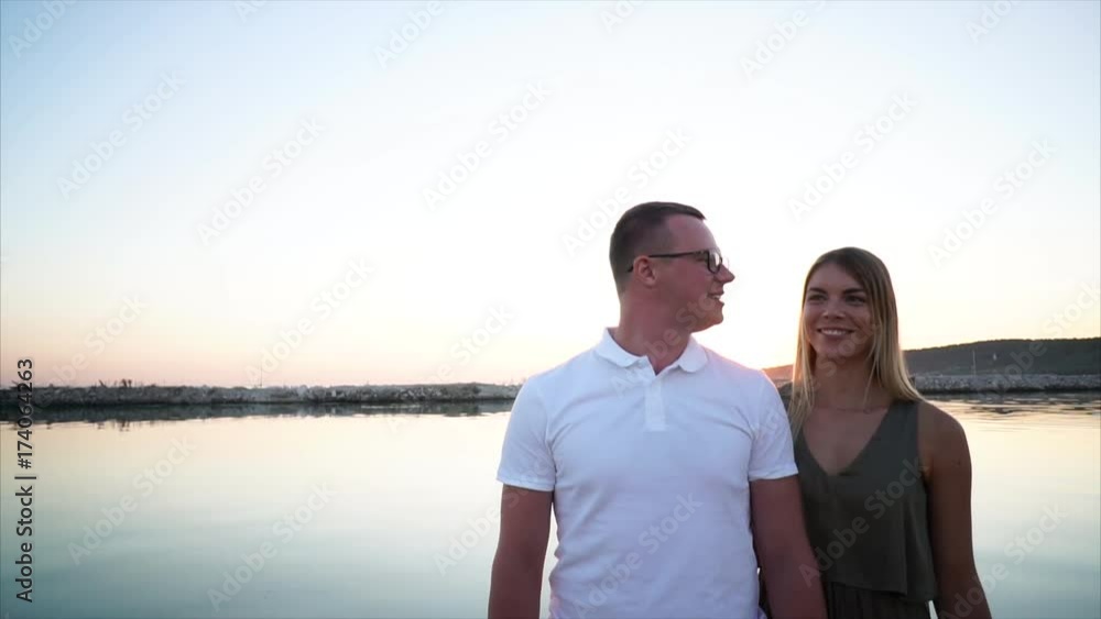 Beautiful couple is spending their time on a shore and enjoying the romantic evening. Warm summer evening by the river. Beautiful couple is spending their time on a shore and enjoying the romantic evening. Warm summer evening by the river.