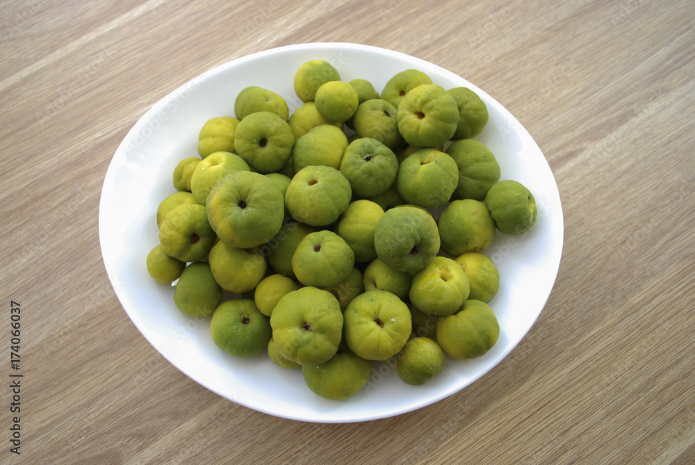 Chaenomeles japonica (known as Maule's quince) green and yellow fruits on the white plate. Wooden background. Chaenomeles japonica (known as Maule's quince) green and yellow fruits on the white plate. Wooden background.