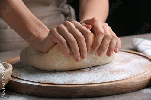 Female chef kneading dough on wooden board at kitchen