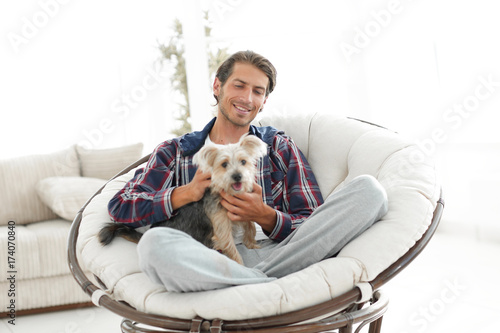 handsome guy with a dog sitting in a large armchair. © ASDF